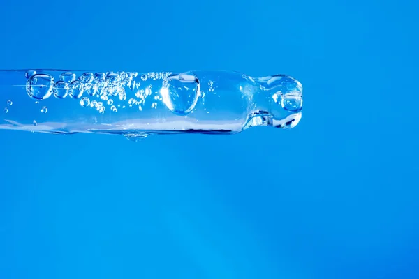 Διαφανής ορός προσώπου σε γυάλινη πιπέτα με φυσαλίδες σε μπλε φόντο. Υγιές προϊόν φροντίδας του δέρματος με κολλαγόνο closeup. Υγρό καλλυντικό τζελ σε σταγονόμετρο. Ιατρική έρευνα έννοια — Φωτογραφία Αρχείου