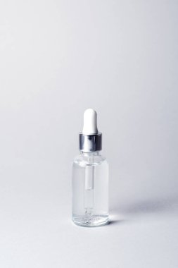 Gri arka planda gümüş ve beyaz pipetli şeffaf cam şişe. Düşürme şişesinde yüz serumu. Yakın plan. Markalaşma için kozmetik ürün. Minimum konsept. Dikey fotoğraf, boşluğu kopyala