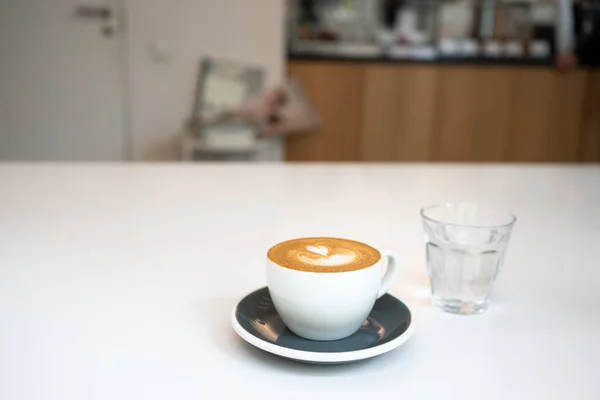 Secangkir kopi dan segelas air di meja putih di kafe. Cappuccino segar di pagi hari. Tampilan depan Stok Foto Bebas Royalti