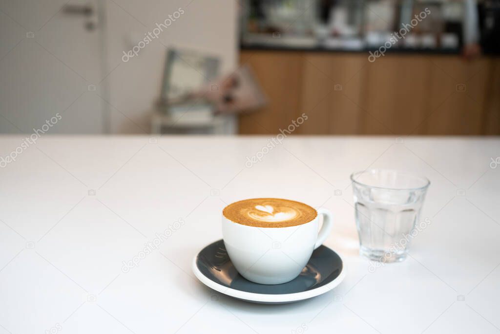 Cup of coffee and glass of water on white table in cafe. Fresh cappuccino at morning. Front view