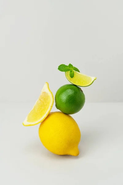 Fresh bright yellow lemon, green juicy lime slice, mint leaf balanced on grey background. Ripe citrus fruits on top of each other. Healthy diet superfood. Ingredients for lemonade. Minimal still life. — Stock Photo, Image