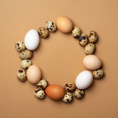 Paskalya kompozisyonu. Bej arka planda tavuk ve bıldırcın yumurtaları. Taklit alanı olan yuvarlak çerçeve. Üst manzara, düz uzanma