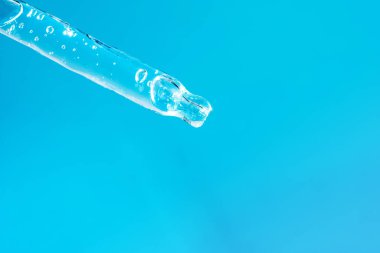 Yüz serumu ve açık mavi arka plan makrosu köpüklü cam damlası. Cilt bakımlı şeffaf pipet. Aloe vera jel ya da reklam için gerekli yağ. Hyaluronik asit. Ön görünüm
