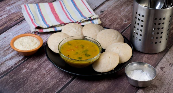 Banyard darı unundan yapılmış idlis tabağı. Tahta bir masada sambhar ve hindistan cevizi turşusu var..