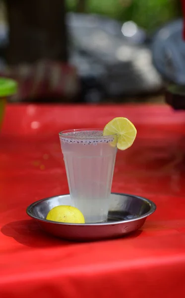 Bir bardak limon suyu ya da çelik bir tabakta limonata ve bir parktaki kırmızı plastik bir tabağın üzerinde bir parça limon.