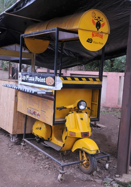 Old yellow scooter used as a prop for road side stall selling fast food and pizzas. Location: Nashik, Maharashtra, India. Date - July 03 2022: 