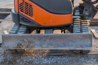 Önünde toprak kalıntıları olan metal dikdörtgen bir bıçakla turuncu bir kazıcı ya da buldozer parçası. İnşaat alanında beton yüzeyde duran makine