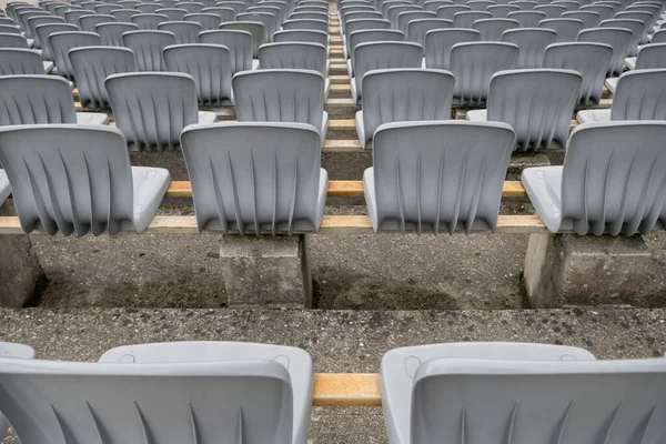 A group of gray plastic seats installed in rows on the street area with ribbed backs going into perspective, fixed on metal rectangular crossbars located on alternating concrete bollards