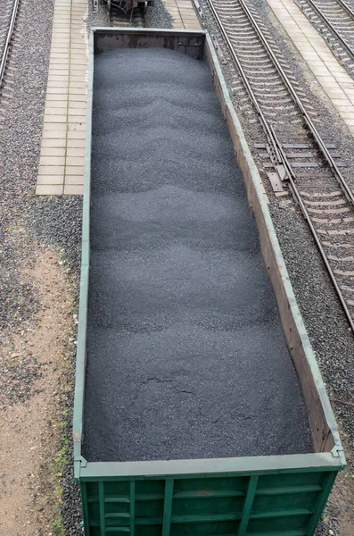 Yeşil metal yük vagonunun tepesine eşit miktarda kömür yığılmış, rayların üzerinde boş demiryolu rayları arasında duran, aralarındaki boşluklar beton kiremitlerle kaplı, yukarıdan bir manzara..