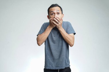Şaşırmış ve şok olmuş Asyalı bir adam stüdyo arka planında elleri izole bir şekilde ağzını kapatıyor.
