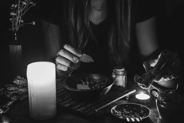 A witch casting a spell at night in candlelight, holding a laurel leaf in her hands