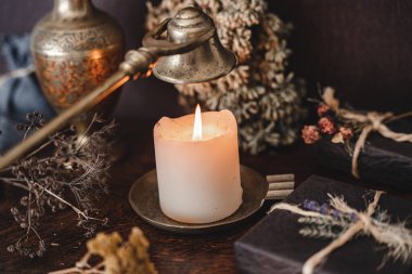 Wiccan cadısı, antika altın sarısı fitil söndürücüyle beyaz mum alevini söndürüyor. Bir cadının mihrabında büyü yapmak
