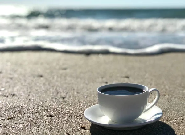 A white cup of americano coffee on the beach. Best vacation concept. Relaxation and inspiration concept, daytime, zen, mental health.