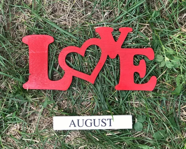 Sign Love August on natural green grass background. Concept of the last summer month.