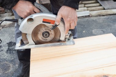 Erkeklerin elleri elektrikli testereyle tahtaları keser.