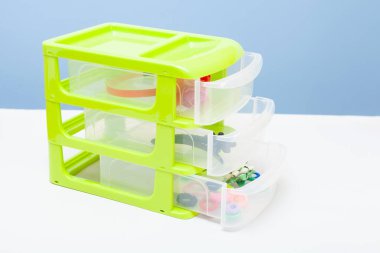 Çekmeceli plastik yeşil şeffaf depolama kabı. Saç tokaları ve elastik bantlar var.