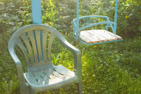 Блакитні дитячі гойдалки на подвір'ї в променях заходу сонця. Поруч стілець для дорослих — стокове фото