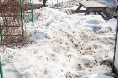 Bahçedeki kirli eriyen kar. Eski ahşap bir masa görünüyor.