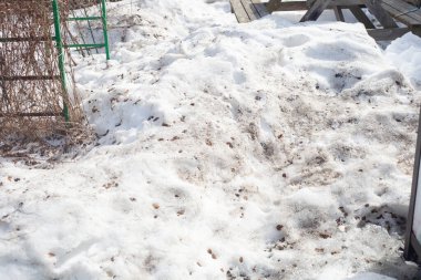 Bahçedeki kirli eriyen kar. Eski ahşap bir masa görünüyor.