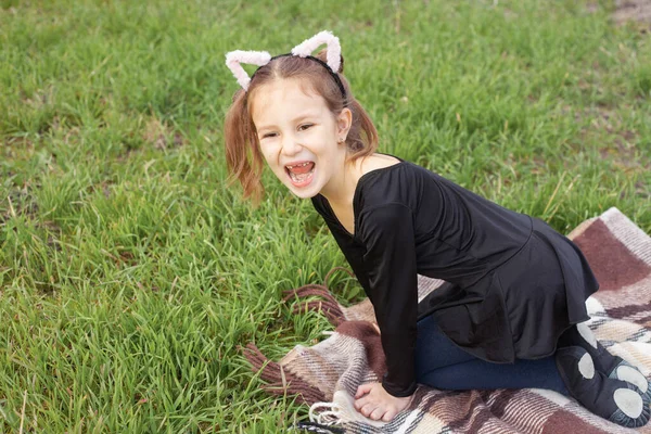 Девочка с розовыми ушами на голове дугообразно шипит, как кошка на траве — стоковое фото
