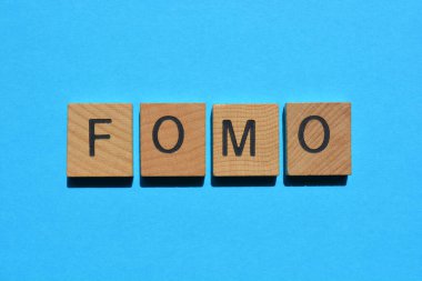 FOMO kısaltması, ahşap alfabe harflerinde kaybolma korkusu mavi arka planda izole edilmiş.