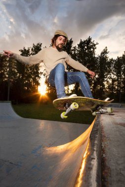 Kaykaycı arka planda güzel bir günbatımı ile kaykay pistinde yükseğe çıkıyor.