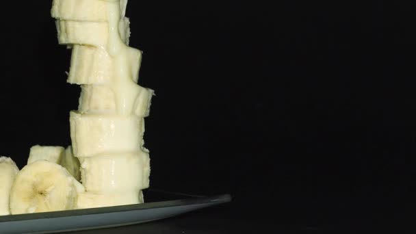 Gecondenseerde melk in een dunne stroom wordt gegoten in een schaal met gesneden bananen — Stockvideo
