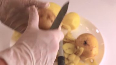 Beyaz eldivenli kadın ellerinin yakın çekimi. Normal bıçakla çiğ patates soyarlar.