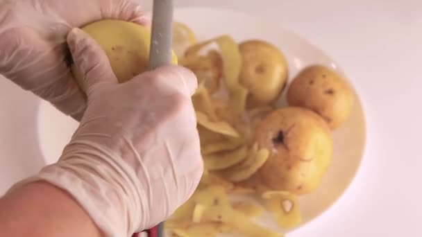 Närbild av händer skalar rå potatis. Skalet avlägsnas i en spiral — Stockvideo