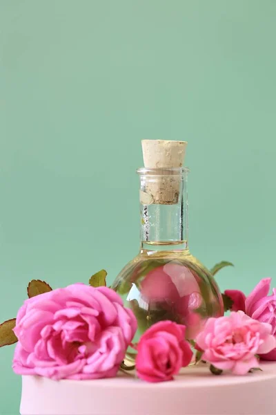 Óleo essencial de rosa. Aromaterapia e massagem.Óleo de rosa e rosas rosa colocados em um pódio rosa em fundo verde claro.. — Fotografia de Stock
