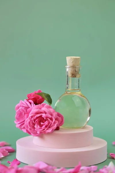 Niezbędny olejek różany. Aromaterapia i masaż.Olej różany i różowe róże ustawione na różowym podium na jasnozielonym tle. — Zdjęcie stockowe