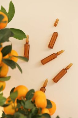 C vitamini ampulleri ve bej arka planda mandalina meyve çalıları. Ampuller ve C vitamini organik kozmetik ile Serum. Sağlık ve Güzellik. 