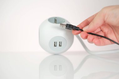 USB adaptörü. USB bağlantısı olan bir soket. Şarj istasyonu. Şarj aletlerindeki USB kablosunu ve teknolojiyi de ekleyin. Kare beyaz soket ve telefon şarjlı eller.