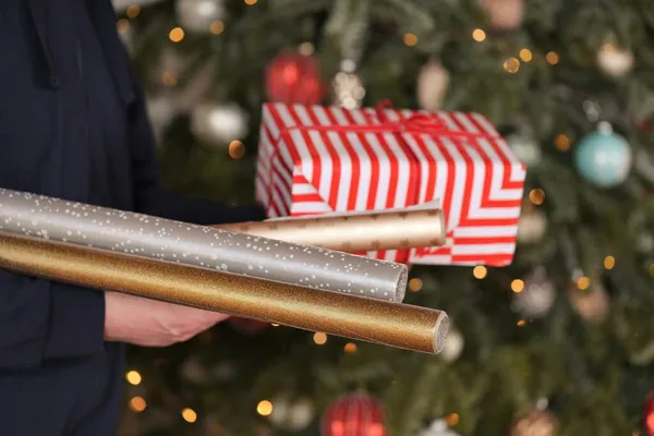 Papel de presente. Rolos de papel de presente de Natal em mãos no fundo da árvore de Natal. Embalagem para presentes de Natal e Ano Novo. surpresas para o Natal. — Fotografia de Stock