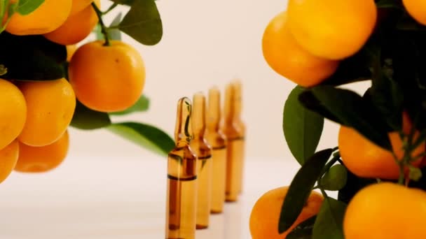 Vitamine C. Mesotherapie serum met vitamine C. Glazen ampullen en mandarijnen fruitstruiken op beige achtergrond — Stockvideo