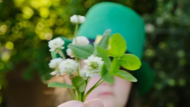 St.Patrick s Day.Girl in green leprechaun hat with clover bouquet on green blurred spring garden background.Irish spring festive carnival. — Stock Video