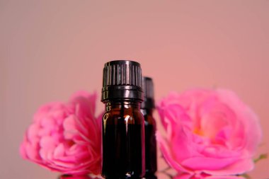 Gül özü yağ, romaterapi ve kozmetik konsepti. Cam kahverengi şişeler ve pembe arka planda pembe gül çiçekleri..