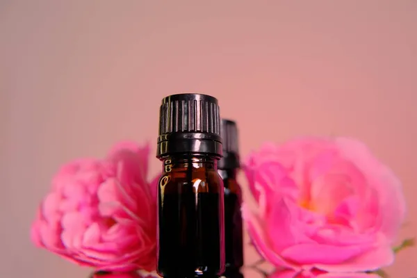 Aceite esencial de rosa.Concepto de aromaterapia y cosmética. Conjunto de botellas de vidrio marrón y flores rosas rosadas sobre fondo rosa. — Foto de Stock