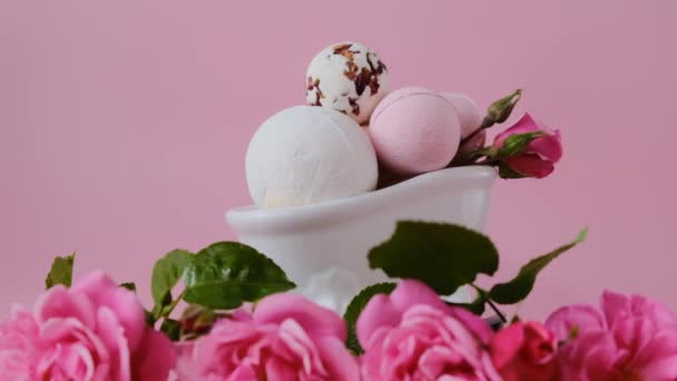 Bombas de banho com extrato de rosa em um banho decorativo de cerâmica e rosas rosa em um fundo rosa claro. Rotação. Beleza e aromaterapia. Flower Bath Bombs.Organic vegan eco cosméticos. — Vídeo de Stock