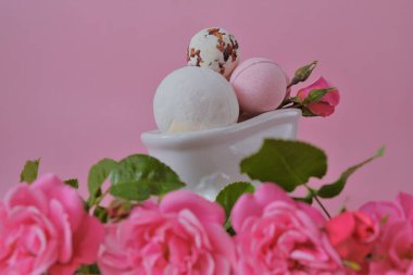Seramik banyoda gül özlü banyo bombaları ve pembe arka planda pembe güller. Pembe banyo bombaları ve pembe gül. Çiçek Banyo Bombaları. Güzellik ve aromaterapi. Organik vegan kozmetik ürünleri.