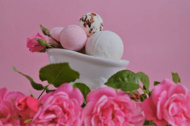 Seramik banyoda gül özlü banyo bombaları ve pembe arka planda pembe güller. Pembe banyo bombaları ve pembe gül çiçekleri. Çiçek Banyo Bombaları. Güzellik ve aromaterapi.. 