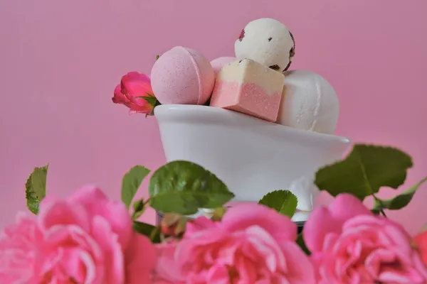 Bombas de banho com extrato de rosa em um banho de cerâmica e rosas cor-de-rosa em um fundo rosa.Bombas de banho rosa e flores rosa rosa. Flower Bath Bombs.Beleza e aromaterapia. Cosméticos veganos orgânicos. — Fotografia de Stock