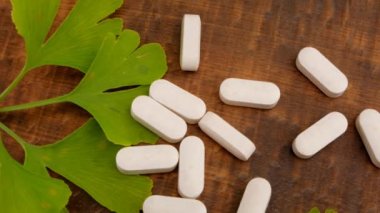 Ginkgo biloba hapları. Tahta arka planda ginkgo özü ve ginkgo yapraklı homeopatik beyaz haplar. Alternatif tıp ve homeopati..
