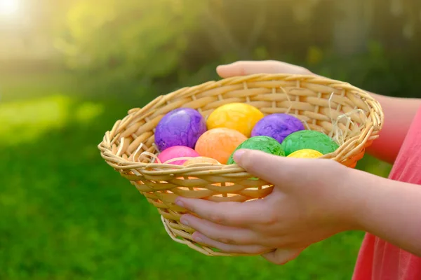 Пасхальное яйцо. Пасхальные яйца, посаженные в корзину в детские руки на зеленом фоне травы. Собираю яйца. Религиозные традиции праздника. Цветные пасхальные яйца. Пасхальный символ. — стоковое фото