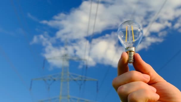 Light bulb in hand on Pylon of the electricity power line background.Electricity concept. electricity line. Power lines on blue sky background — Stock Video