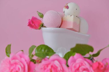 Seramik bir banyoda gül özlü banyo bombaları ve pembe arka planda pembe güller. Çiçek Banyo Bombaları. Organik vegan kozmetik ürünleri. Güzellik ve aromaterapi.