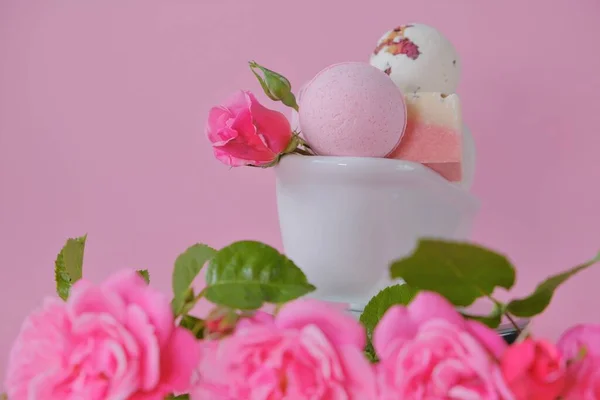 Bombas de banho com extrato de rosa em um banho de cerâmica e rosas rosa em um fundo rosa. Flower Bath Bombs.Cosméticos veganos orgânicos. Beleza e aromaterapia. — Fotografia de Stock