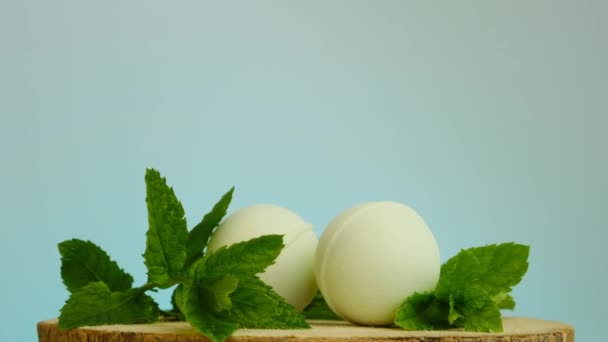 Bombes de bain avec extrait de menthe. Rotation. Beauté et aromathérapie.Bain vert bombes et brins de menthe poivrée sur une scie à bois coupée sur un fond bleu clair. — Video