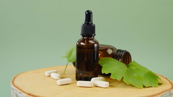 Ginkgo biloba özü tabletlerde ve sıvı ginkgo biloba, açık yeşil arkaplanda ginkgo yaprakları. Rotasyon. Alternatif tıp ve homeopati.. — Stok video