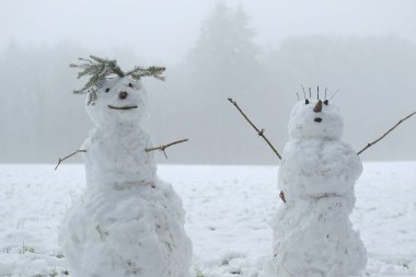 Karlı bir arazide kardan adam çifti. Şimdi de kardan adam figürü. Kar heykeli. Kardan adam yapmak için. Kış eğlencesi ve oyunlar. Noel ve Yeni Yıl şenliği. Kış mevsimi
